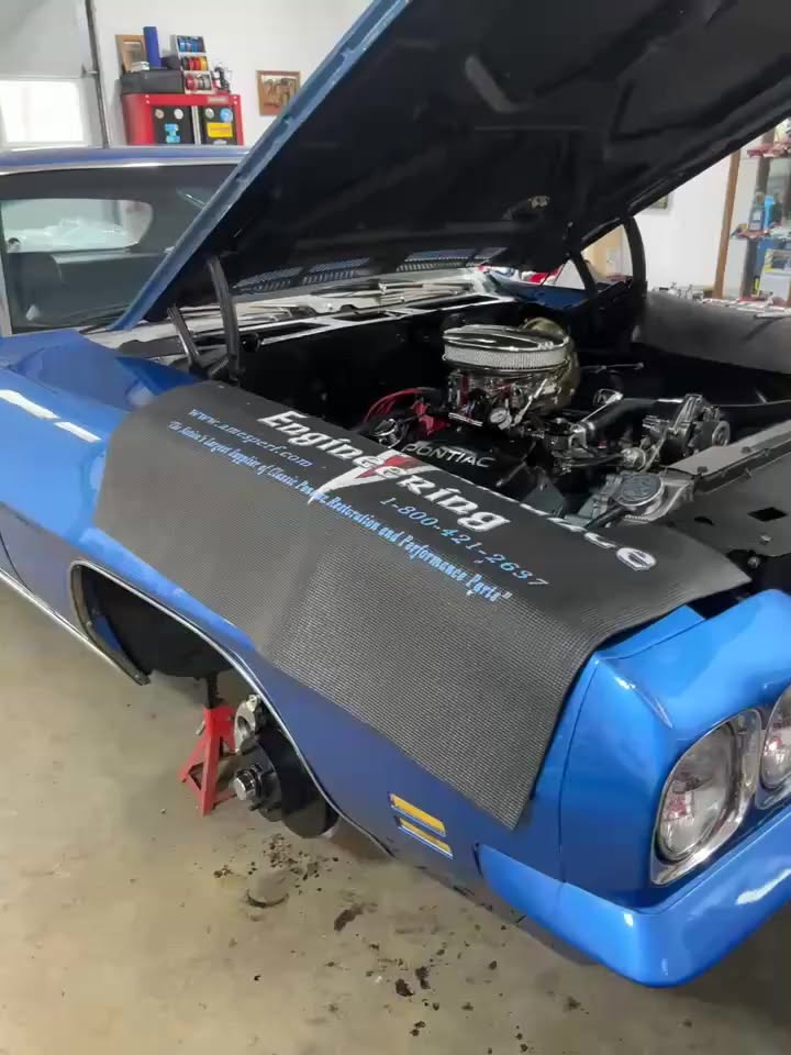 A blue Pontiac with its hood open in the company’s original shop video